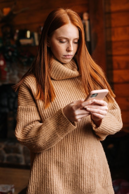 Triste giovane donna che digita un messaggio sul telefono cellulare mentre si autoisola durante le vacanze invernali