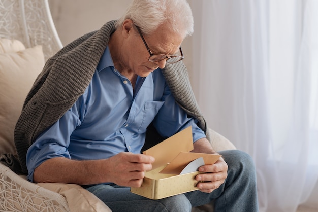 Triste simpatico uomo anziano che gira le sue vecchie lettere e ricorda la sua giovinezza mentre era solo