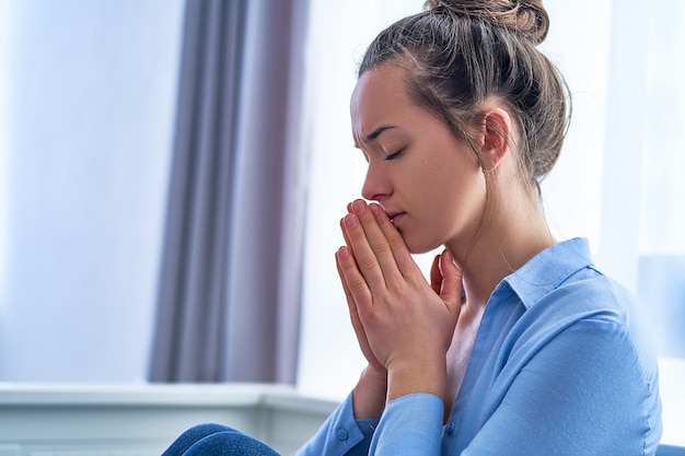 Triste solitaria depressa donna senza speranza con le mani giunte e gli occhi chiusi persi nei pensieri