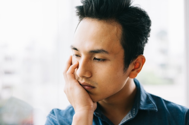 Triste uomo asiatico vicino alla finestra