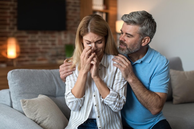 Triste uomo caucasico di mezza età con barba abbraccio calmo piangendo moglie infelice nell'interno del soggiorno