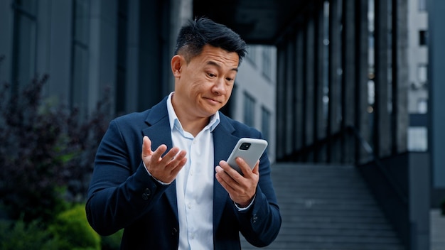 Triste uomo d'affari asiatico in città problema mobile CEO di mezza età datore di lavoro navigazione telefono sensazione sconvolta