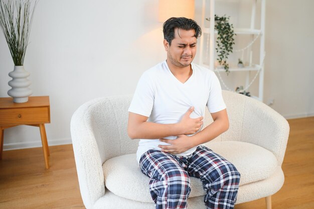 Triste uomo esausto di etnia indiana e araba tiene le mani sullo stomaco fa le grimace per il dolore allo stomaco soffre di avvelenamento spasmo problemi di stomaco