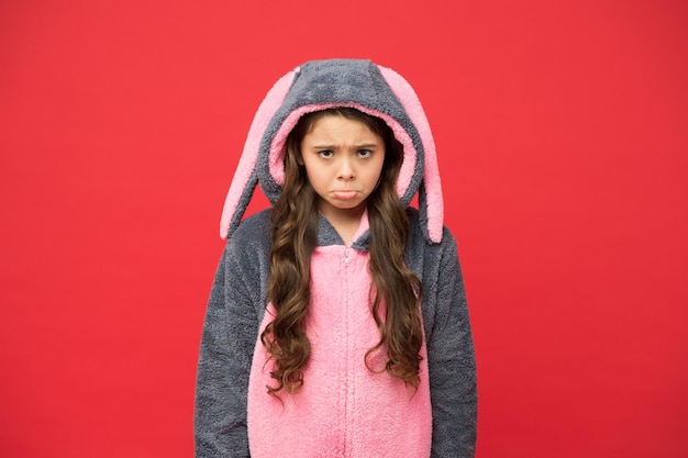 Tristezza Riposo e relax Simpatico coniglietto su sfondo rosso Ruolo del personaggio animale del bambino Ragazza splendida in costume da coniglio Bambino in kigurumi di coniglio Ragazza triste in pigiama da coniglio Concetto di depressione