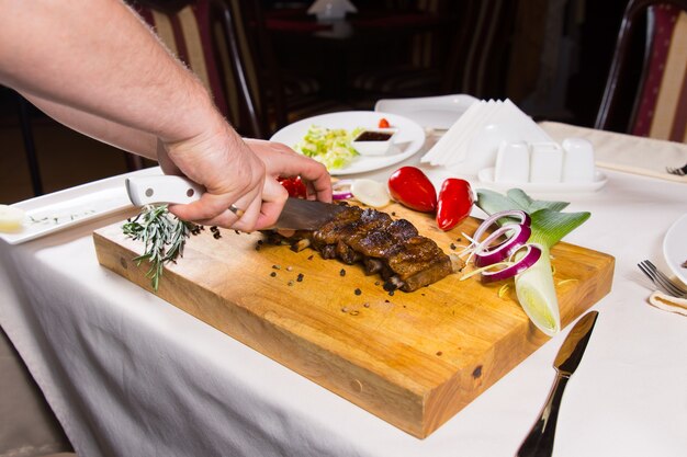 Tritare la carne cotta in pezzi sul tavolo bianco utilizzando un tagliere di legno.