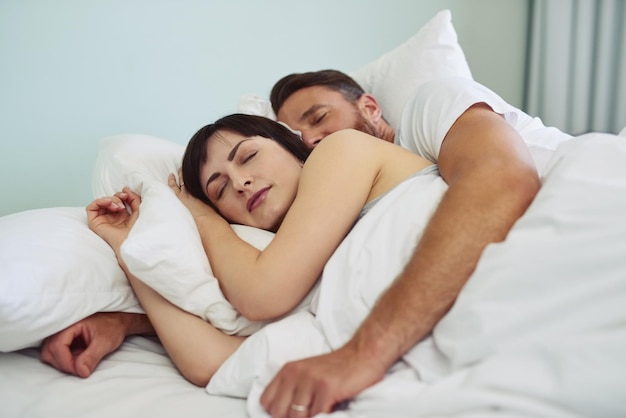 Troppo comodo per alzarsi dal letto Inquadratura di una giovane coppia rilassata che dorme abbracciata a letto durante le ore mattutine