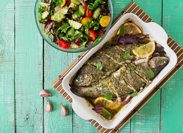 Trota al forno e insalata fresca su un fondo di legno luminoso