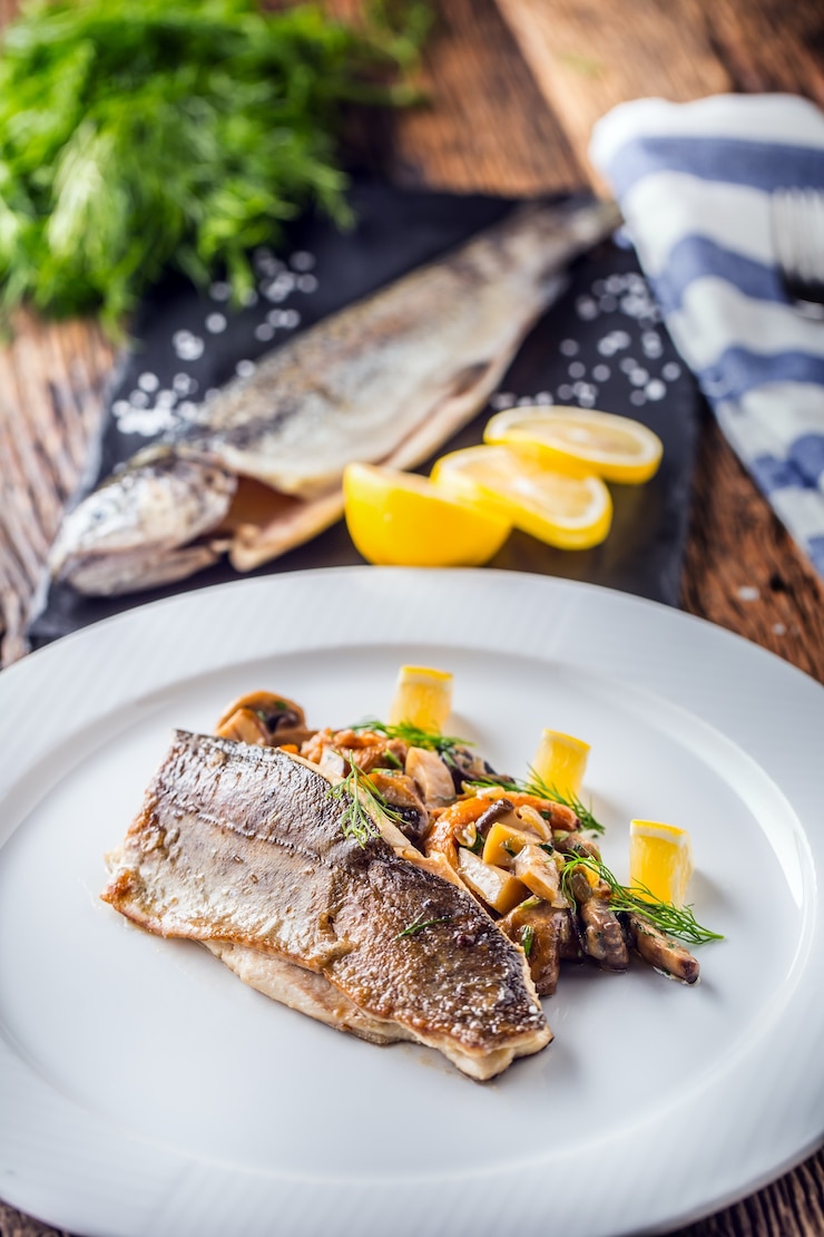 Foto trota di pesce con funghi e verdure sul piatto in hotel o ristorante.