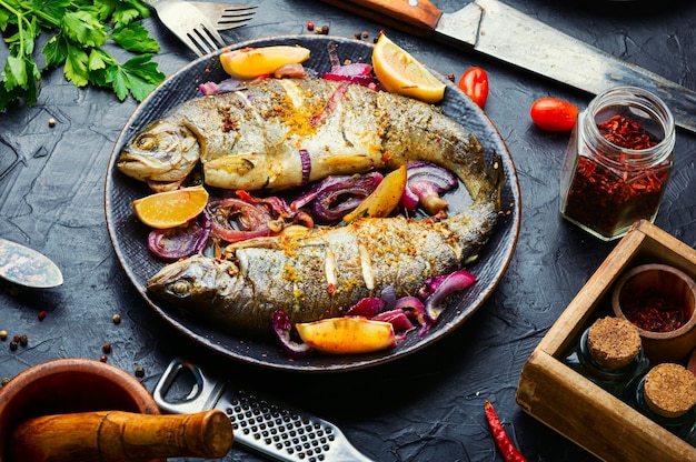 Trota iridea alla griglia con limone e cipolla sul piatto. Pesce arrosto