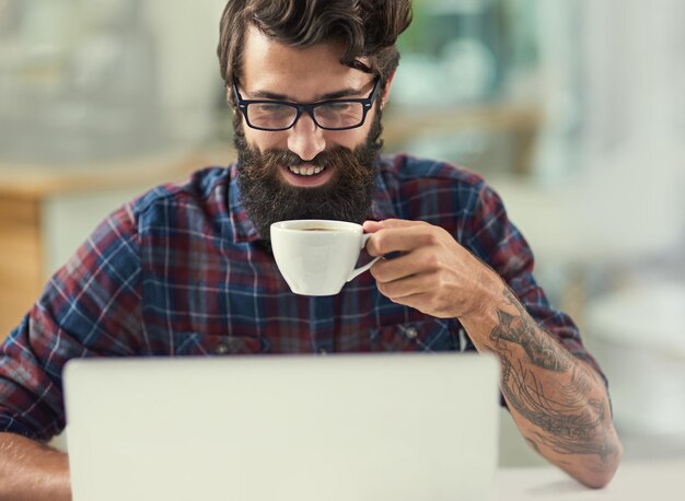 Trova l'ispirazione di cui hai bisogno per avere successo Inquadratura di un designer che beve un caffè mentre lavora al suo laptop