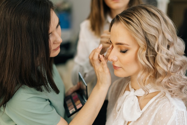 Truccatore professionista che fa il trucco del viso mentre il parrucchiere fa la pettinatura per una giovane donna