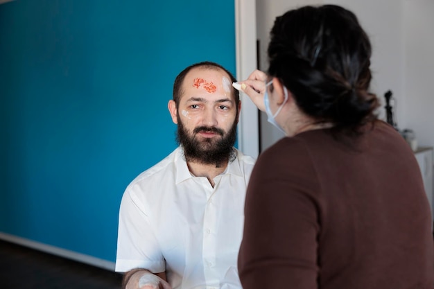 Truccatrice che trasforma l'uomo in zombie con effetti speciali, sangue e spaventoso costume drammatico. Creando un aspetto da cadavere infetto da non morti con occhi da diavolo crudeli e una faccia spaventosa assetata di sangue.