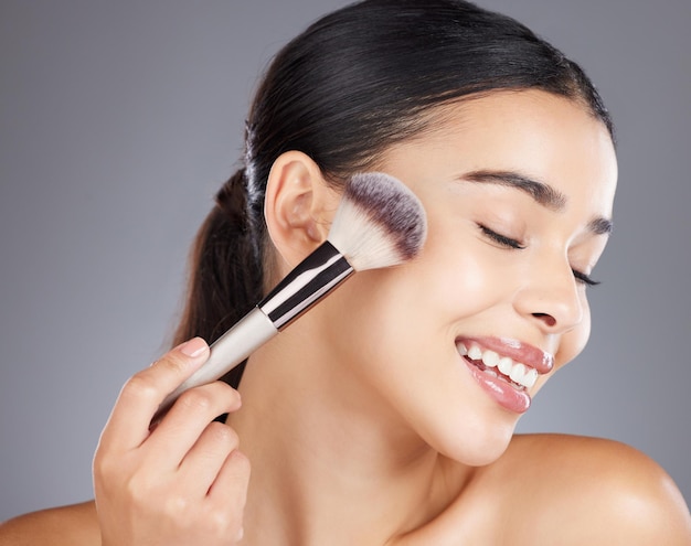 Trucco bellezza o donna con un pennello per cosmetici per il viso o prodotti per la cura della pelle di lusso Viso estetico o felice bella ragazza modello sorrisi toelettatura nella routine di cura di sé isolato su sfondo studio