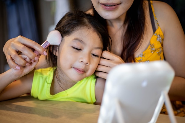 Trucco della madre per la figlia in camera. Concetto di famiglia felice.