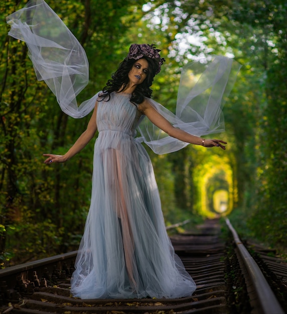 Trucco della sposa morta nel vestito nel tunnel all'interno di una foresta con binari del treno