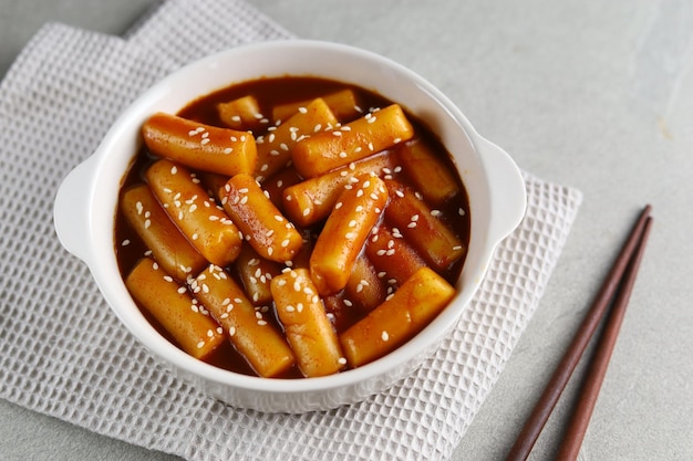 Tteokbokki con sesamo bianco in una ciotola bianca con sfondo grigio