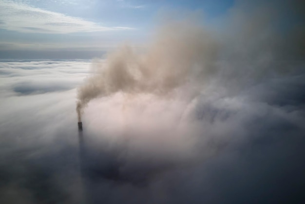 Tubi alti della centrale a carbone con fumo nero che si muove verso l'alto sopra le nuvole atmosfera inquinante Produzione di energia elettrica con il concetto di combustibile fossile