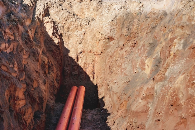 Tubi fognari arancioni in una trincea Posa di comunicazioni nel terreno durante la costruzione dell'edificio