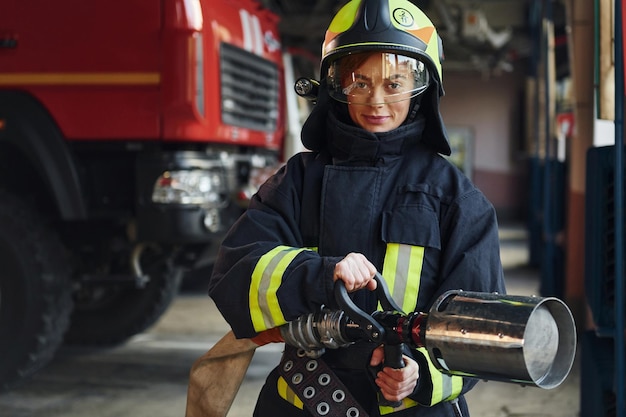 Tubo in mano Vigile del fuoco femminile in uniforme protettiva in piedi vicino al camion