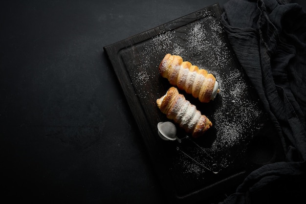 Tubuli al forno ripieni di panna montata su una tavola da cucina in legno nero vista dall'alto