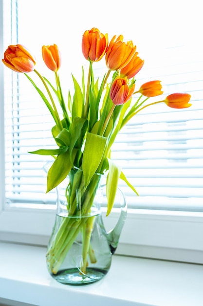 Tulipani arancioni gialli luminosi primaverili in vaso di vetro sul primo piano del davanzale