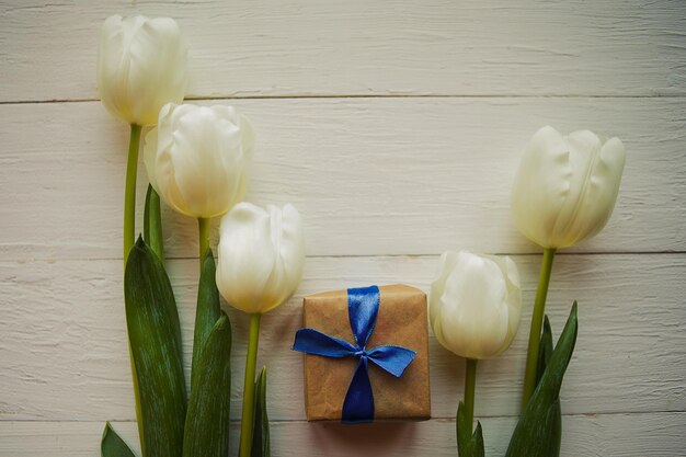 Tulipani bianchi e scatola regalo su sfondo di legno biglietto di auguri per la Pasqua o la Giornata delle Madri Copia lo spazio per il testo