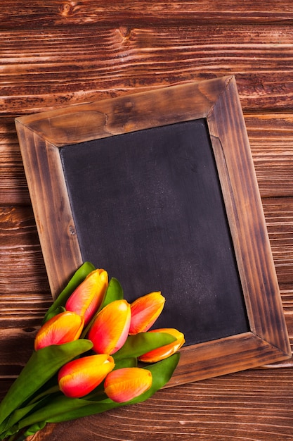 Tulipani con lavagna su uno sfondo di legno - auguri di primavera