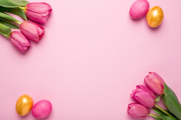 Tulipani delle uova di Pasqua e dei fiori di rosa e dell'oro su una superficie rosa