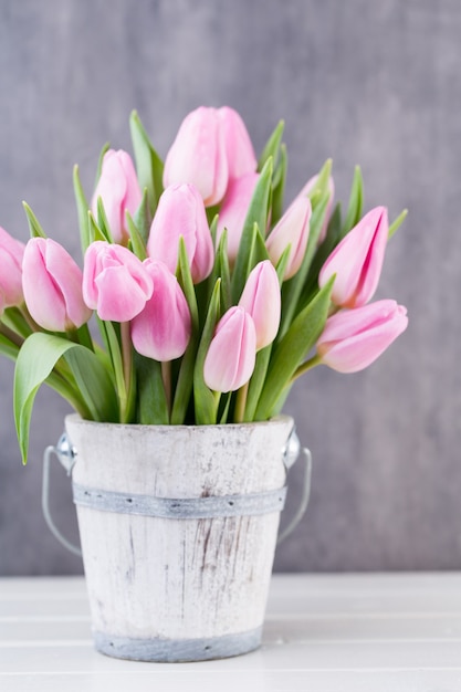 Tulipani di Pasqua di primavera nel secchio su sfondo bianco vintage.