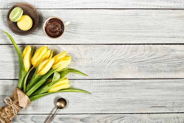 Tulipani gialli, cioccolato e macarons su un tavolo di legno bianco