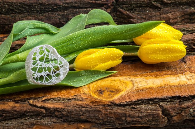 Tulipani gialli freschi con gocce d'acqua su una tavola di legno naturale.