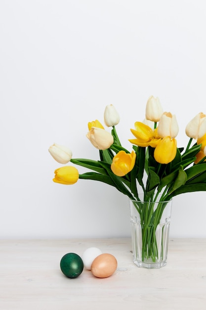 Tulipani gialli in un vaso e uova multicolori sulla tavola di Pasqua