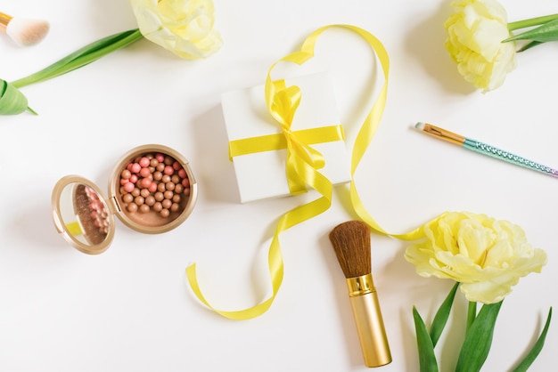 Tulipani gialli una confezione regalo con un nastro giallo e un fiocco cosmetici decorativi su sfondo bianco Elegante fashion blogger piatto