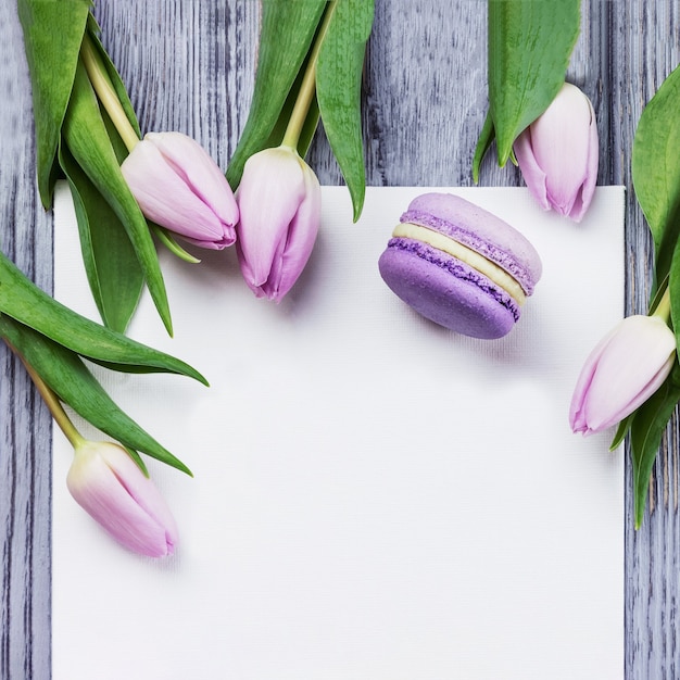 Tulipani, macaron viola e foglio bianco su un tavolo di legno grigio