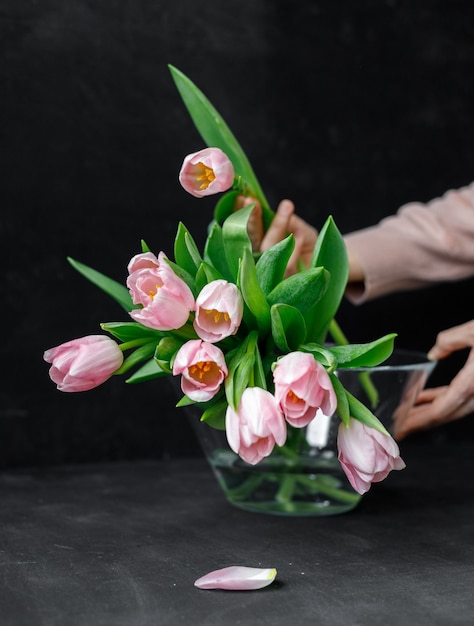 Tulipani rosa con foglie verdi in un vaso di vetro una donna che tiene i tulipani nelle sue mani fioraio fioraio festa della mamma bouquet regalo per l'8 marzo bouquet per una ragazza per il suo compleanno bouquet di tulipani