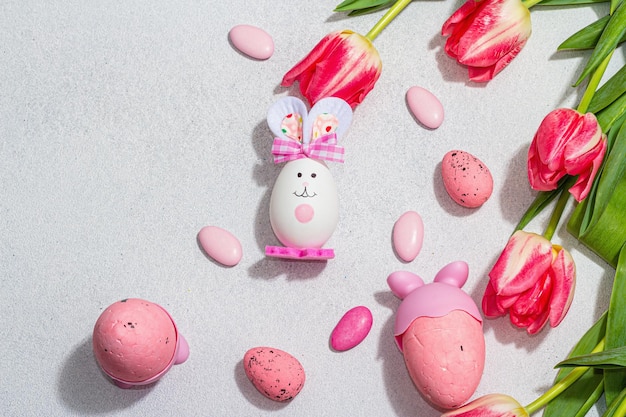 Tulipani rosa con uova di Pasqua e conigli su sfondo di cemento di pietra chiara Biglietto d'auguri per il concetto festivo piatto con vista dall'alto di ombre chiare e scure