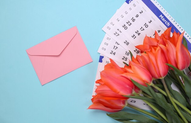 Tulipani rossi, busta e un calendario mensile su sfondo blu. Vista dall'alto