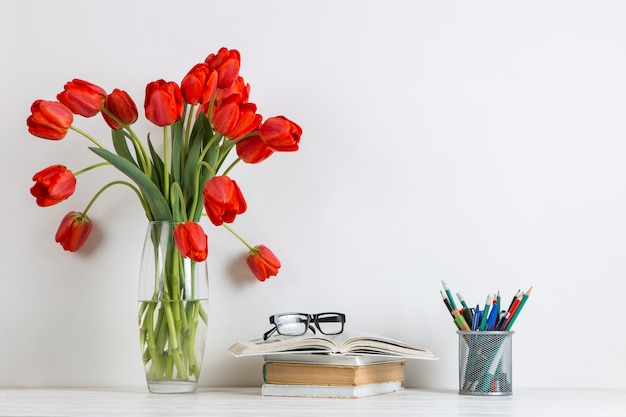 Tulipani rossi in un vaso, libri e materiale scolastico su bianco.