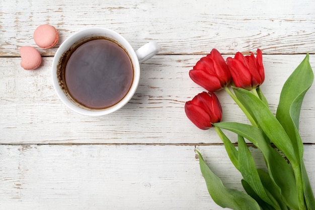 Tulipani rossi, tazza di caffè sul tavolo in legno bianco