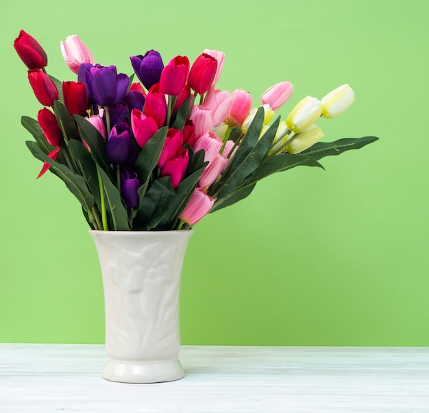 Tulipani variopinti in vaso sul fondo verde di verde della parete della tavola