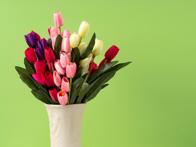 Tulipani variopinti in vaso sul fondo verde di verde della parete della tavola