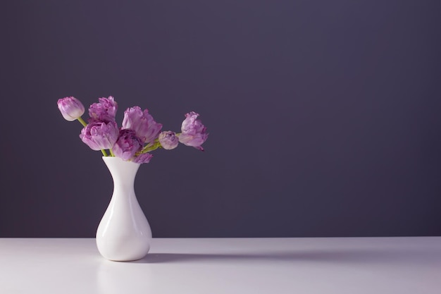 Tulipani viola in vaso bianco su sfondo grigio muro