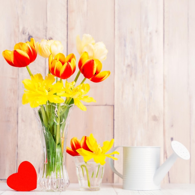 Tulipano floreale in vaso di vetro con cuore saluto annaffiatoio arredamento su tavolo in legno parete di fondo primo piano concetto di design per la festa della mamma