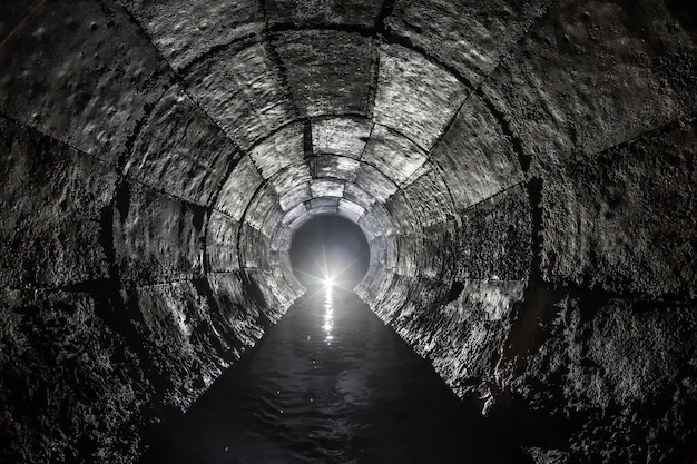 Tunnel di drenaggio rotondo in cemento con acqua costruito con cassaforma Con luce all'estremità Fiume sotterraneo nascosto nel tubo