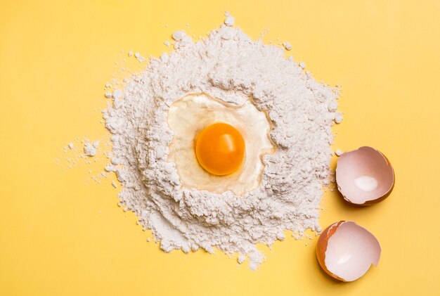 Tuorlo d'uovo rotto sulla farina per la pasta su sfondo giallo. Concetto di cottura.