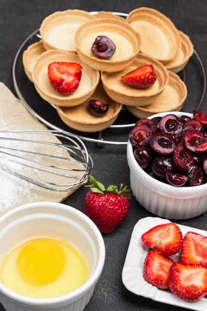 Tuorlo, fragole, ciliegie e tartellette con frutti di bosco su sfondo nero