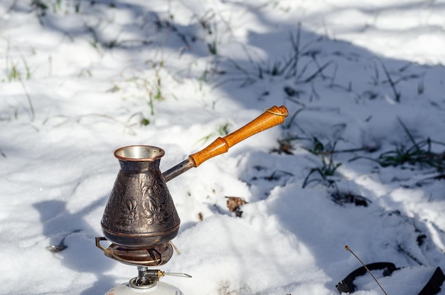 Turco di rame con manico in legno per fare il caffè su uno sfondo di neve nei boschi