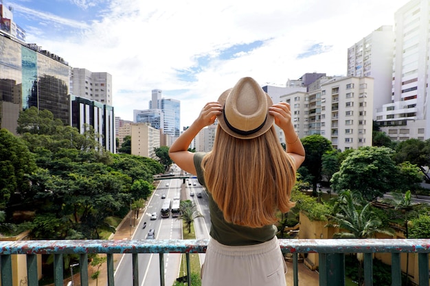 Turismo a San Paolo Vista posteriore della bella ragazza del viaggiatore che tiene cappello godendo della vista del paesaggio urbano di San Paolo Brasile