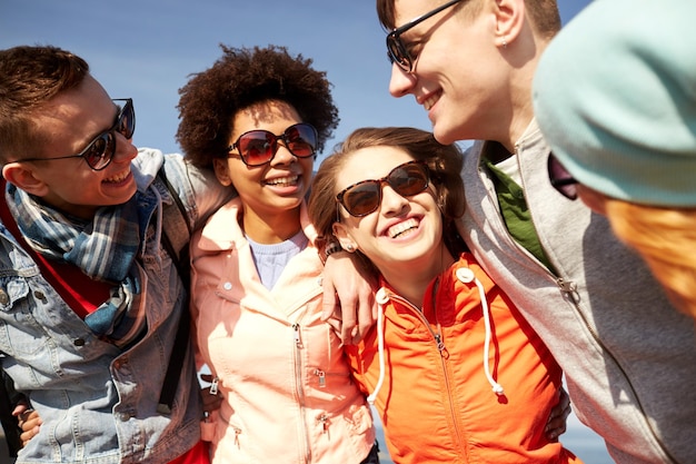 turismo, viaggi, persone, tempo libero e concetto adolescenziale - gruppo di amici felici in occhiali da sole che si abbracciano e ridono sulla strada della città