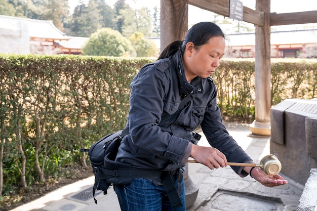 Turista asiatico maschio scavando santuario dell'acqua santa per lavarsi le mani prima di entrare nel tempio Todaiji, Prefettura di Nara, Giappone